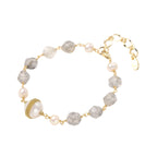 Bracelet with cloudy quartz beads, freshwater pearls, and gold-wrapped baroque pearl centerpiece on white background.