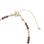 Gold necklace with iridescent baroque pearl pendant, purple amethyst beads, and crystal star charm on cream background
