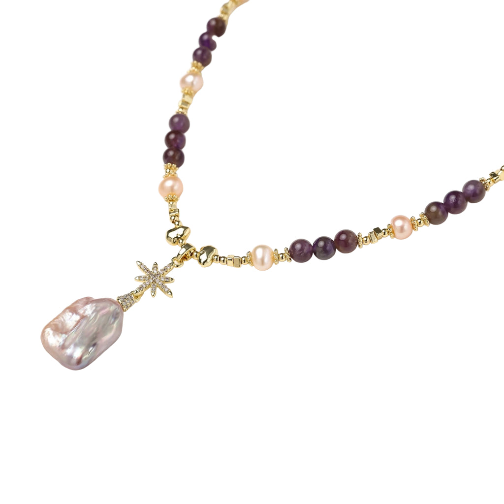 Gold necklace with iridescent baroque pearl pendant, purple amethyst beads, and crystal star charm on cream background