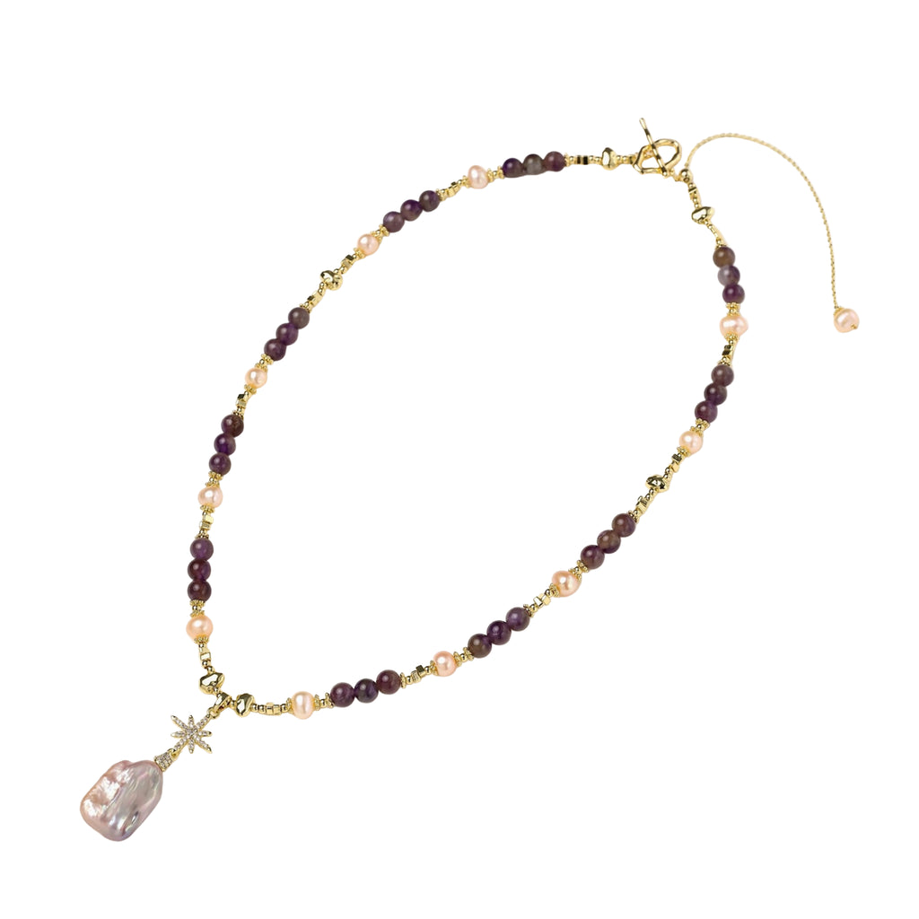 Gold necklace with iridescent baroque pearl pendant, purple amethyst beads, and crystal star charm on cream background