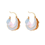 Shell-shaped hoop earrings with iridescent blue-pink enamel and gold trim on cream background