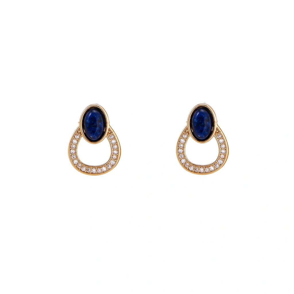 Gold drop earrings with oval lapis lazuli, crystal-paved frame, and iridescent mother-of-pearl teardrop on cream background