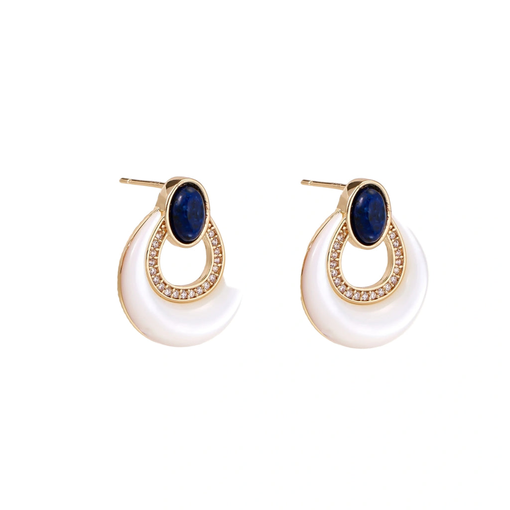 Gold drop earrings with oval lapis lazuli, crystal-paved frame, and iridescent mother-of-pearl teardrop on cream background