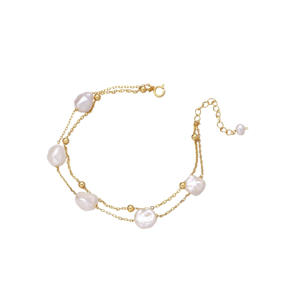 Double-strand gold bracelet with irregular baroque pearls and smooth freshwater pearls on cream background.