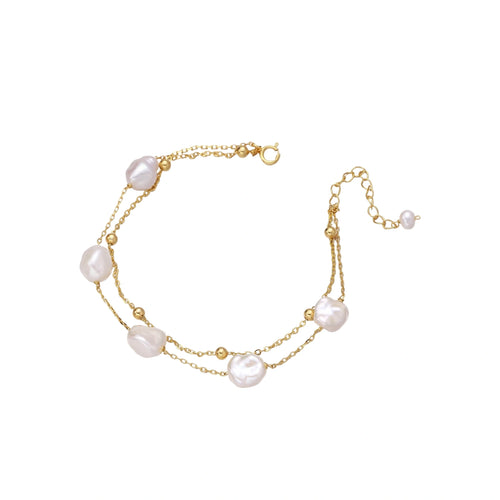 Double-strand gold bracelet with irregular baroque pearls and smooth freshwater pearls on cream background.