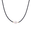 Delicate necklace with black blue sandstone beads and baroque pearl center on white background with gold accents.