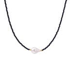 Delicate necklace with black blue sandstone beads and baroque pearl center on white background with gold accents.