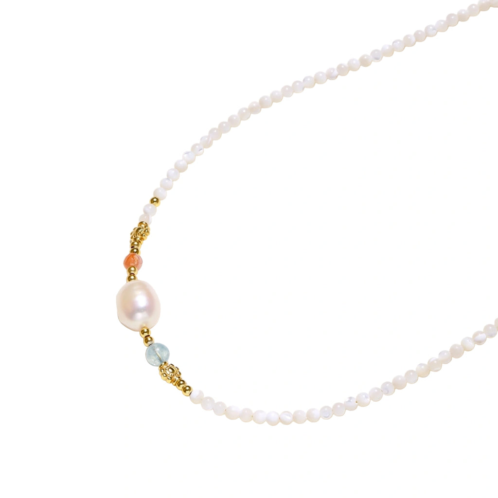 Delicate white beaded necklace with baroque pearl center, gold accents, and coral and aqua gemstones on cream background.
