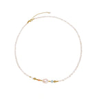 Delicate white beaded necklace with baroque pearl center, gold accents, and coral and aqua gemstones on cream background.