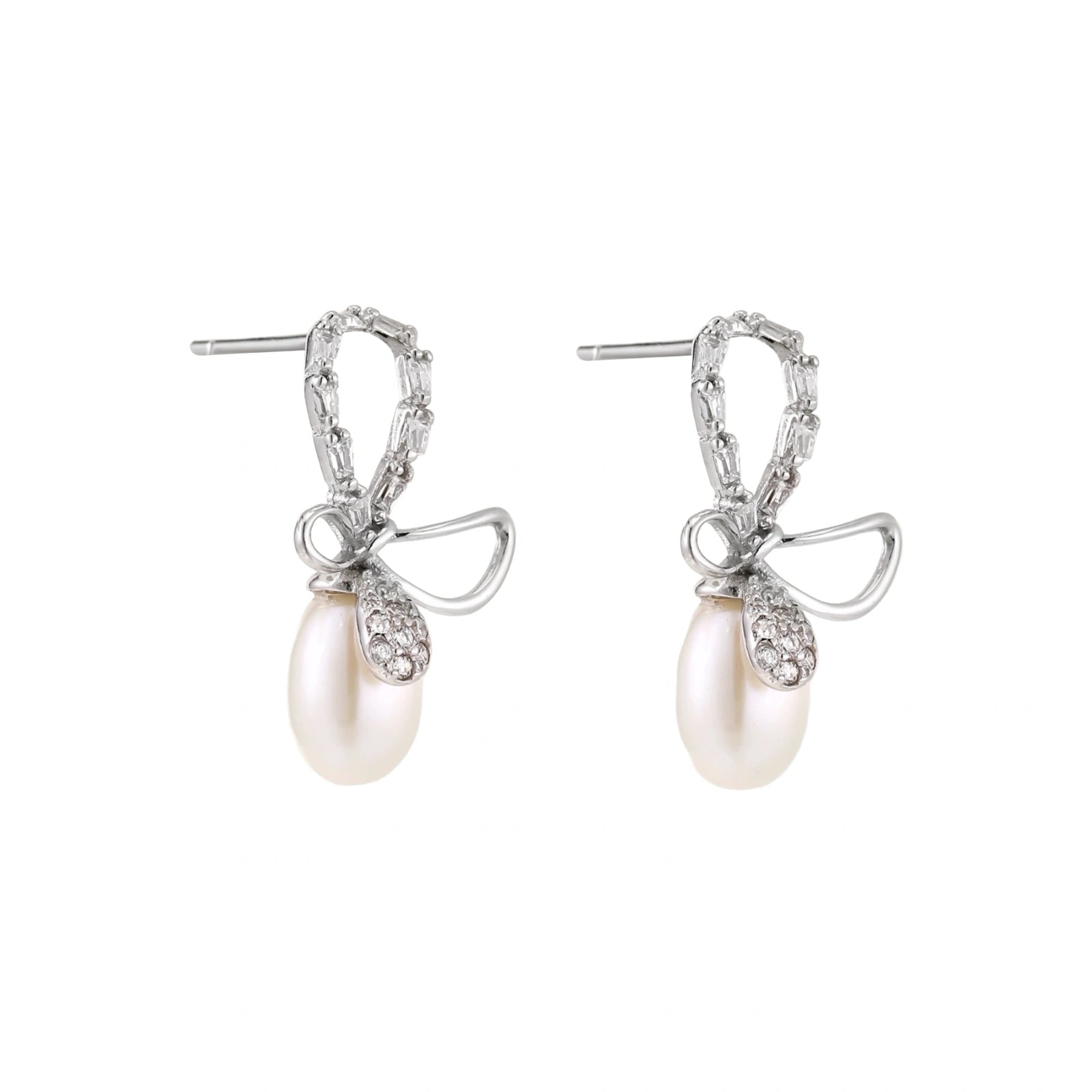 Silver bow-shaped stud earrings with baguette crystals and dangling white freshwater pearls on cream background