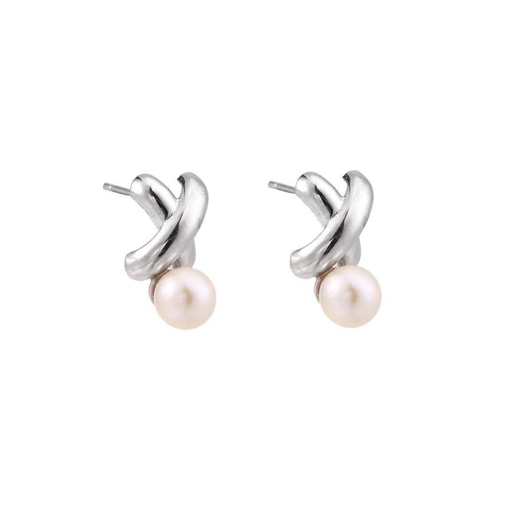 Rhodium-plated silver earrings with twisted X design and freshwater pearl drops on beige background