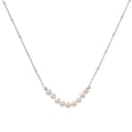 Delicate sterling silver chain necklace with small freshwater pearls arranged in a curved smile arc on cream background.