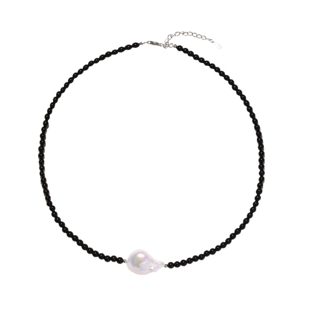 Beaded black agate necklace with iridescent baroque freshwater pearl centerpiece on cream background.