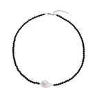 Beaded black agate necklace with iridescent baroque freshwater pearl centerpiece on cream background.
