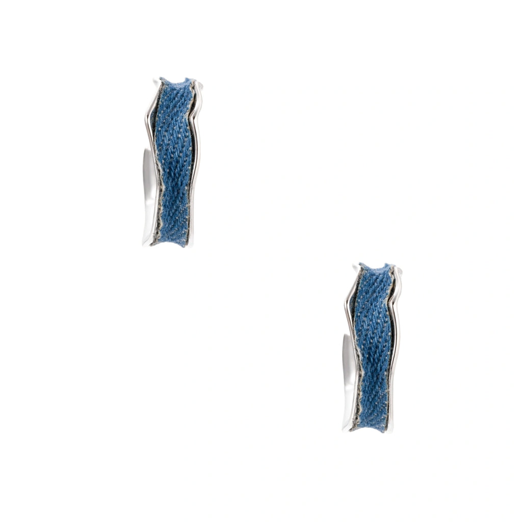 Silver huggie hoops with blue denim fabric inlay strip and polished white gold plated finish on cream background.