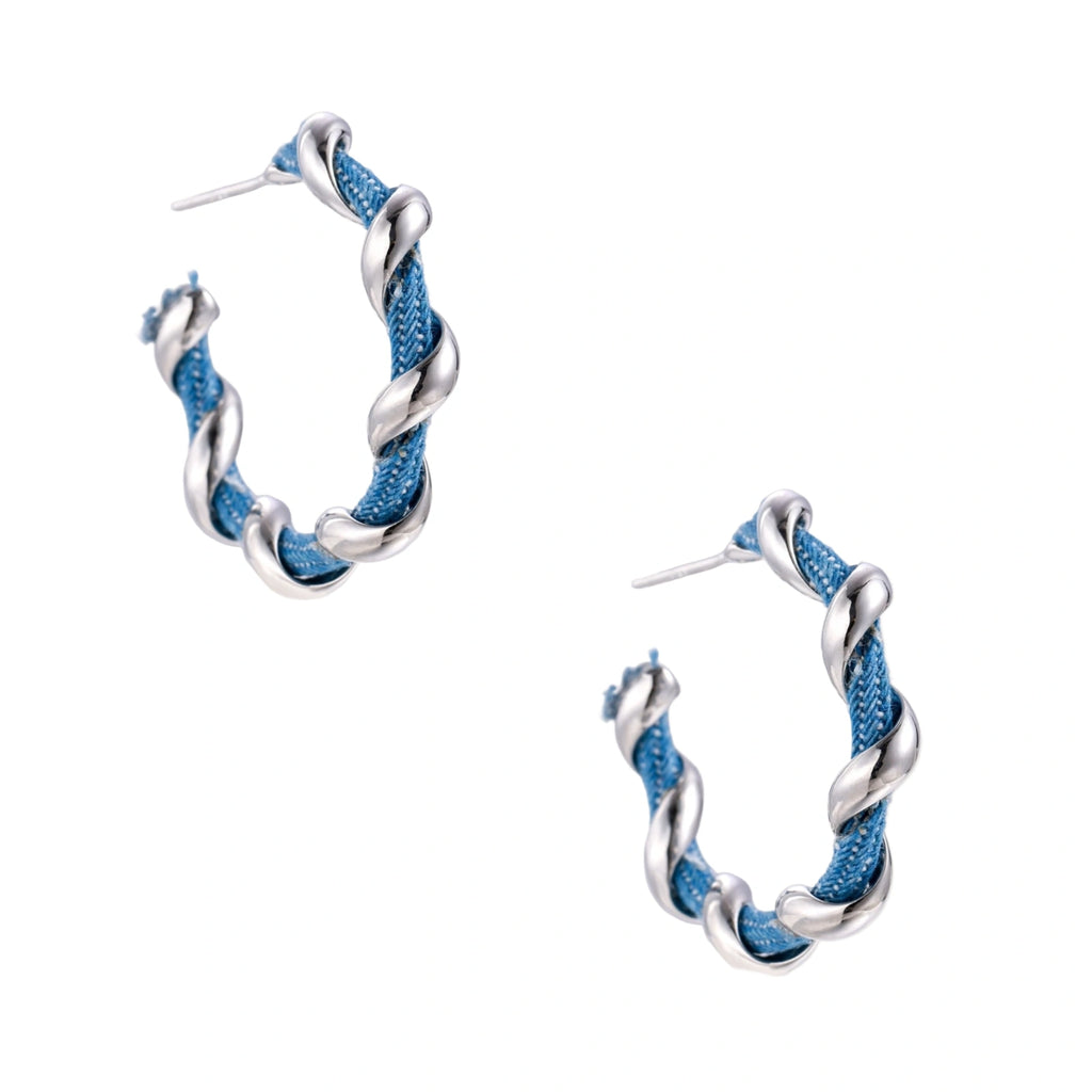 White gold-plated hoops intertwined with blue denim fabric in a twisted rope design on cream background.