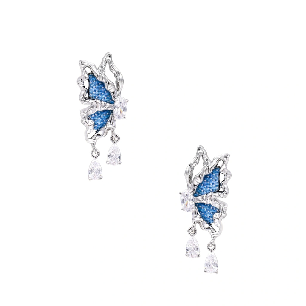 Silver butterfly earrings with blue denim fabric wings and dangling teardrop crystals on cream background