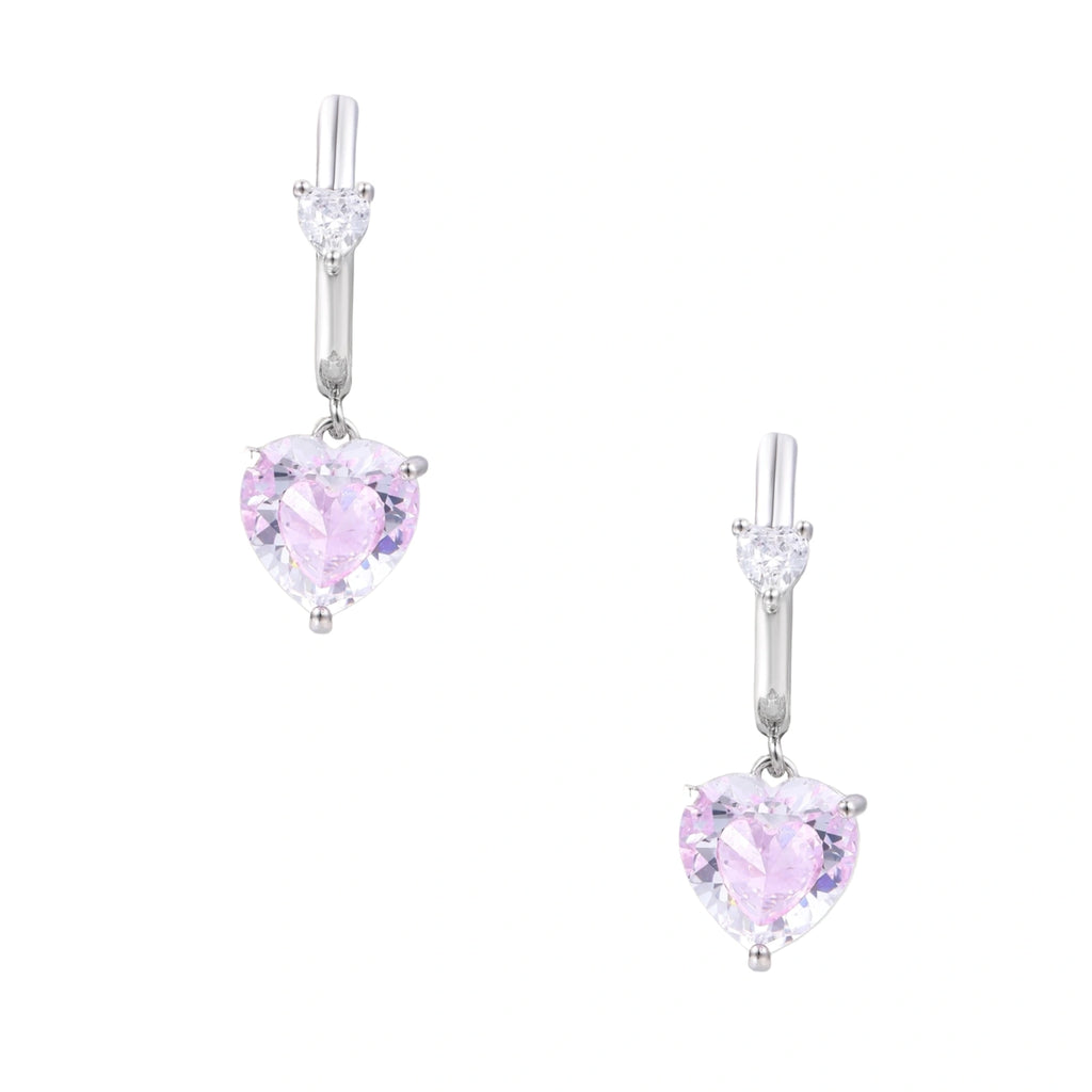 Silver huggie hoops with pink heart-cut zirconia pendants on white background, eco-friendly white gold plated brass