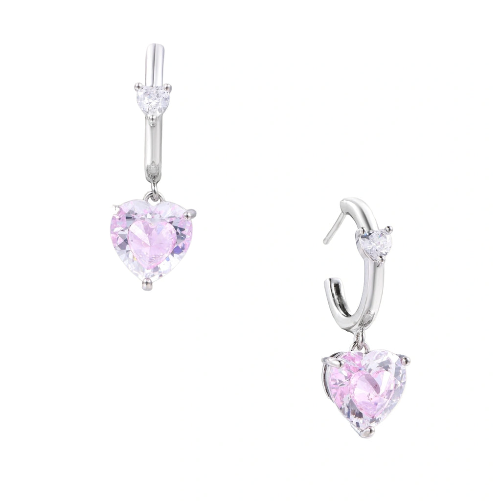 Silver huggie hoops with pink heart-cut zirconia pendants on white background, eco-friendly white gold plated brass