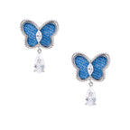 Blue denim butterfly earrings with silver frame and teardrop crystal dangles on cream background
