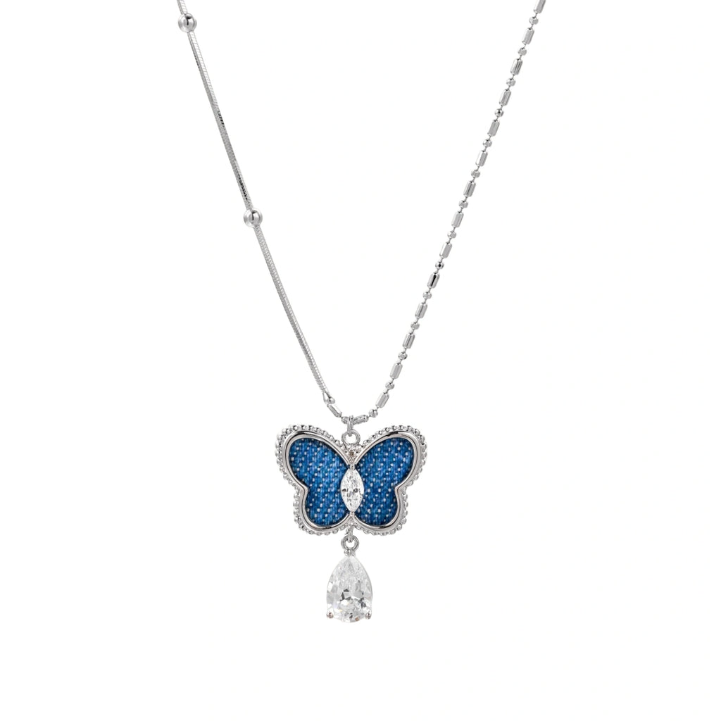 Silver-toned butterfly pendant with blue denim fabric inlay and teardrop crystal on dual-chain necklace