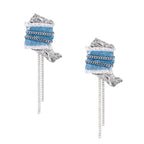 Blue denim fabric earrings with white fringe, silver chains, metallic accents, and dangling chain tassels on cream background.