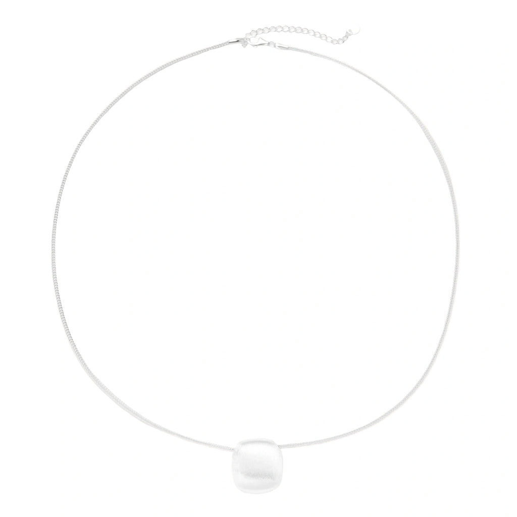 Minimalist brushed sterling silver dome pendant on delicate chain against cream background, showing matte textured finish