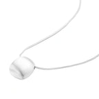 Minimalist brushed sterling silver dome pendant on delicate chain against cream background, showing matte textured finish