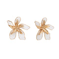 White enamel tropical flower earrings with sculptural gold-plated center and organic petal design on cream background
