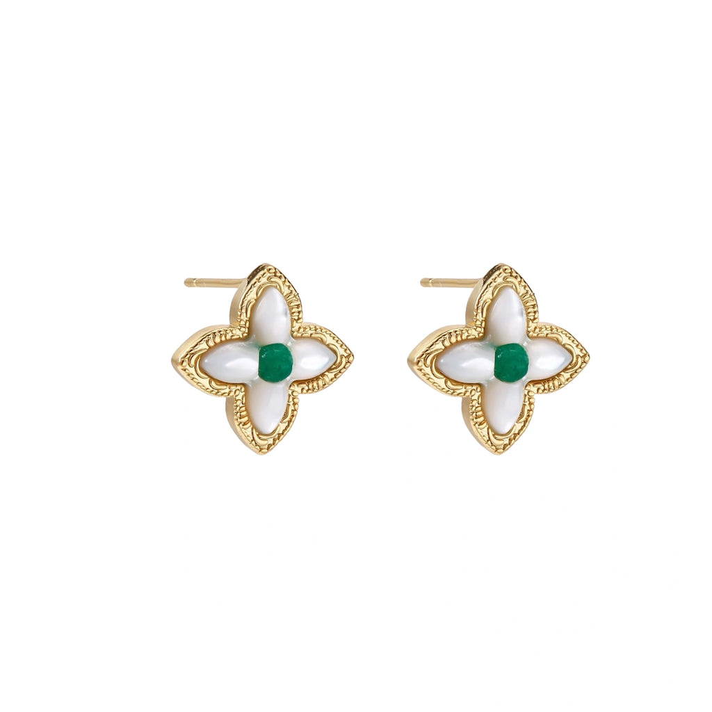 Gold quatrefoil stud earrings with white mother-of-pearl petals and emerald green gemstone center on beige background.
