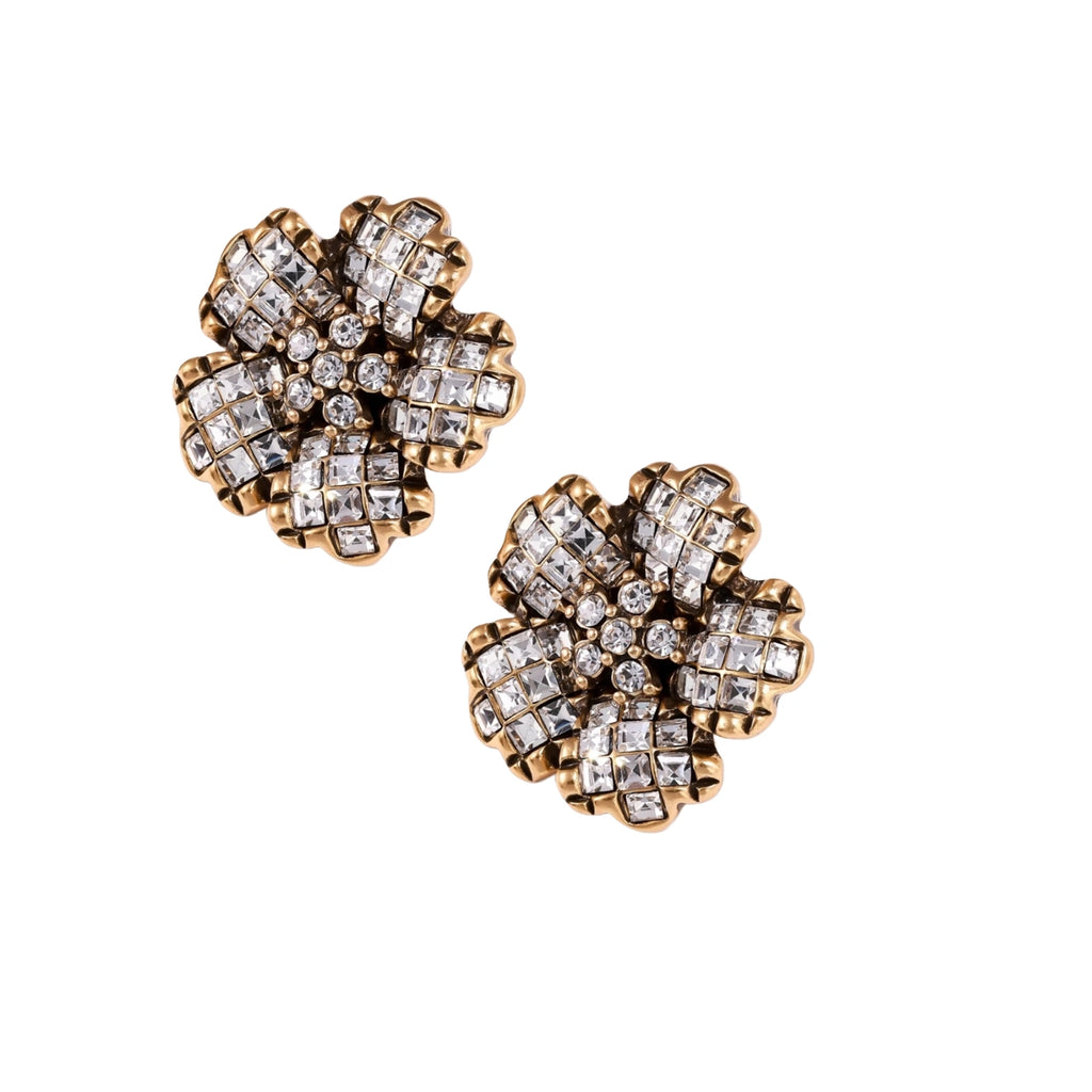 Gold-plated floral stud earrings with geometric zirconia crystals arranged in five-petal design on cream background
