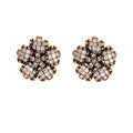 Gold-plated floral stud earrings with geometric zirconia crystals arranged in five-petal design on cream background