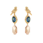 Gold-plated bird stud earrings with iridescent abalone shell medallions and champagne crystal drops on cream background