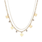 Gold layered necklace set with engraved heart pendants and crystal accents on cream background