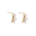 14K gold-plated curved stud earrings with three white freshwater pearls aligned vertically on cream background