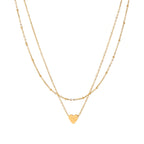 Delicate double-chain gold necklace with tiny heart pendant on cream background