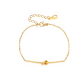 Delicate gold chain bracelet with minimalist bar and centered knot detail on cream background