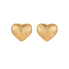 Gold heart-shaped stud earrings with parallel ridged texture on cream background