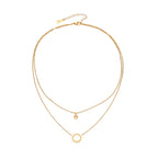 Gold layered necklace set with sunburst and smiley face pendants on delicate chains against white background.