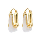 Sculptural gold-plated hoop earrings with flowing curved design and lever-back closure on cream background.