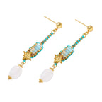 Gold-plated dangle earrings with turquoise threading, star charms, and white pearl beads against cream background.