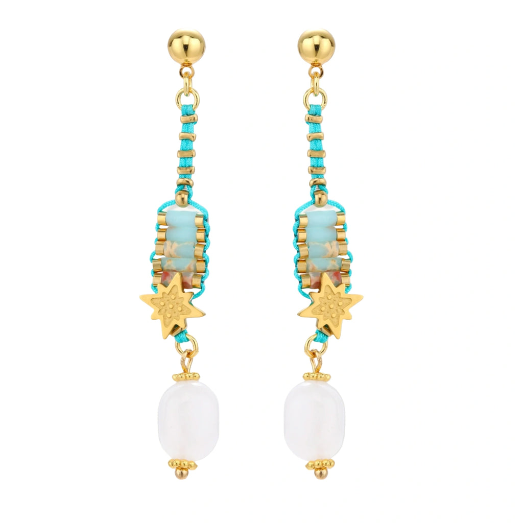 Gold-plated dangle earrings with turquoise threading, star charms, and white pearl beads against cream background.