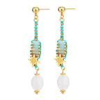 Gold-plated dangle earrings with turquoise threading, star charms, and white pearl beads against cream background.