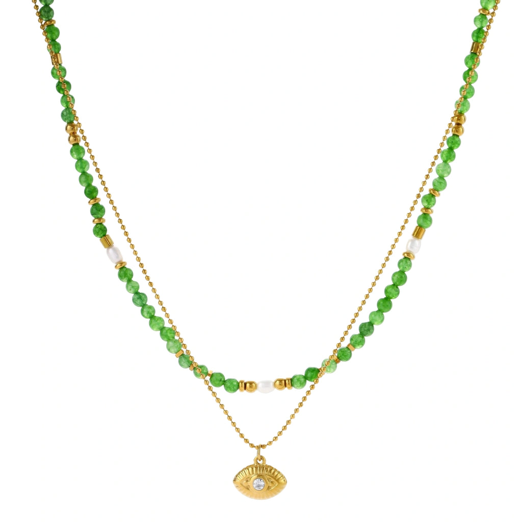 Layered necklace with green stone beads, gold spacers, white accents, and protective eye pendant on cream background.