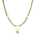 Layered necklace with green stone beads, gold spacers, white accents, and protective eye pendant on cream background.