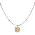 Ornate gold-plated pendant necklace with multicolored gemstone beads in purple, pink and clear tones on white background